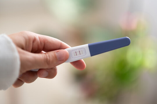 Close-up of hand holding home pregnancy test with two visible lines as positive result. Pregnancy health care, fertility, family planning and conception. Ovulation, fetus, motherhood, childbirth.