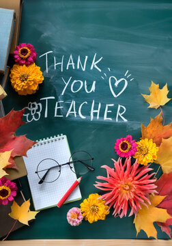 Teacher's day holiday, education concept. chalk inscription "Thank you Teacher" on chalkboard, notebook, pencil, learning books, eyeglass, flowers and autumn maple leaves. top view