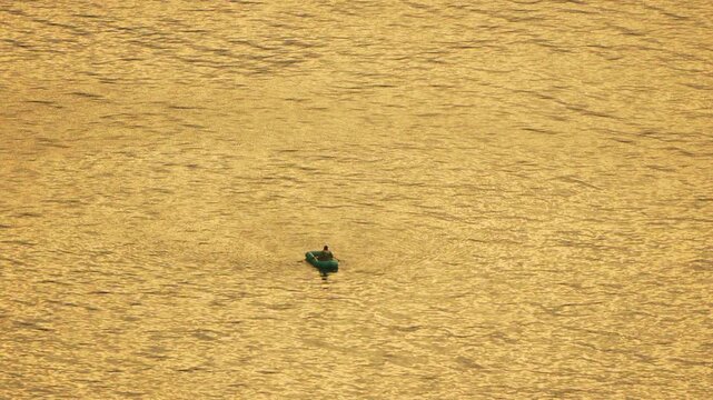 Boat Rowing Sunset Solitary person in an inflatable dinghy rowing across glistening golden water during a serene evening sunset