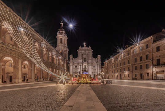 View of the Basilica della Santa Casa illuminated at night with a nativity scene and festive star decorations in the square in Loreto, Marche, Italy.
