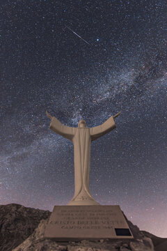 View of the Cristo delle Vette statue with arms outstretched against a starry night sky featuring the Milky Way in Frontignano, Marche, Italy.