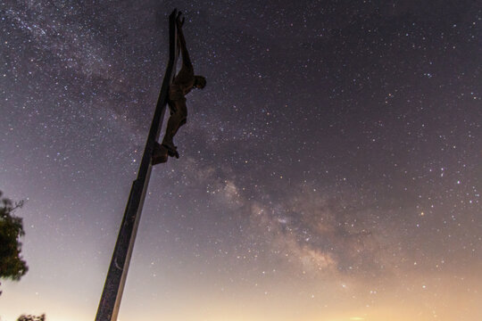 View of a crucifix statue silhouetted against the starry night sky with the Milky Way galaxy visible in San Lorenzo, Marche, Italy.