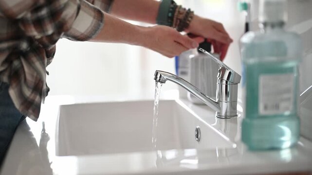 Woman washing hands with soap in white bathroom sink basin during daytime