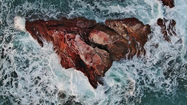 Aerial view of red rocks surrounded by crashing white waves in the Adriatic Sea, Montenegro.