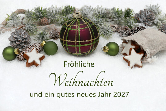 Deutsche Weihnachtsgru&szlig;karte mit Text Fr&ouml;hliche Weihnachten und ein gutes neues Jahr 2027, dekoriert mit Weihnachtskugeln, Tannenzweigen und Zimtsternen im Schnee.