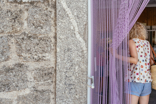 Casual mature woman entering small local shop through beaded curtain in Spanish town