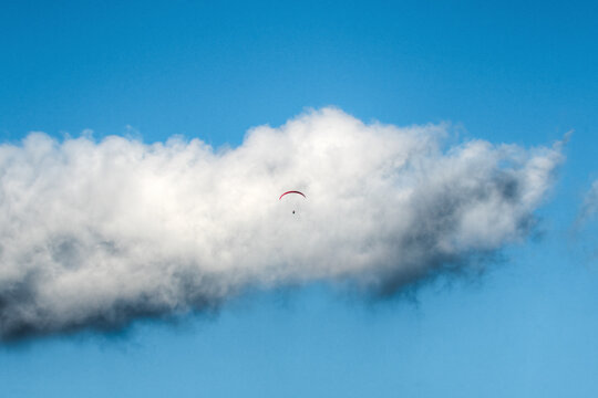 View of a paraglider soaring through the clear blue sky near a large white cloud in Castelluccio, Umbria, Italy.