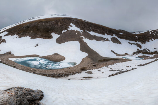 View of the partially frozen Lago di Pilato surrounded by snow-covered slopes and rocky terrain in the Sibillini Mountains in Montemonaco, Marche, Italy.