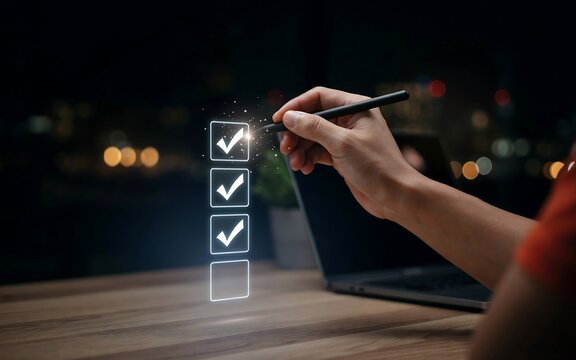 Hand holding a digital pen checking boxes on a virtual task list in a dark office environment