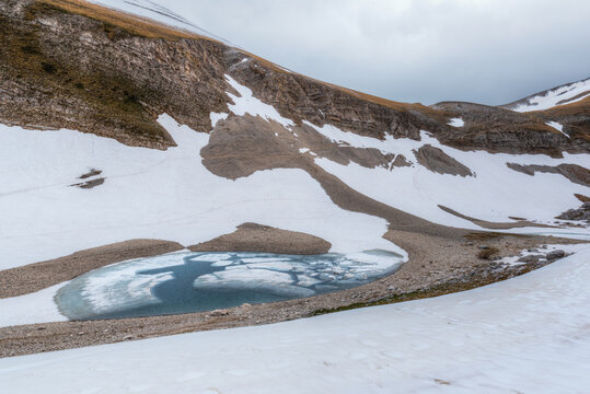 View of the glacial Lago di Pilato surrounded by snow-covered slopes and rocky terrain in Montemonaco, Marche, Italy.