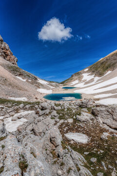 View of the glacial Lago di Pilato surrounded by rocky slopes and patches of melting snow under a clear blue sky in Montemonaco, Marche, Italy.