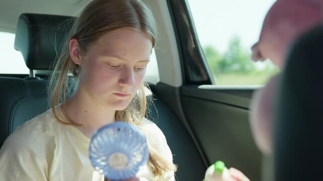 Girl using a handheld fan while traveling by car slow motion holding a stress-relief toy