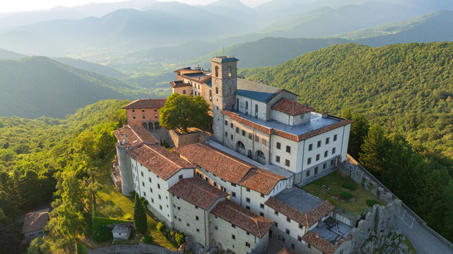 Majestic drone shot displays historic sanctuary of Castelmonte on hilltop. Ancient stone fortification walls and religious architecture stand over Friuli region landscape under clear sky.