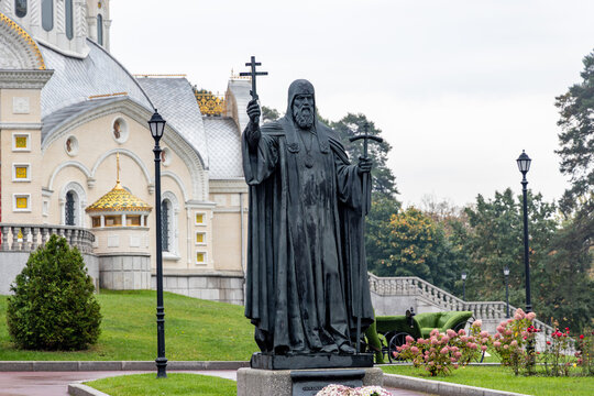 Peredelkino, Russia - September 23, 2026: Bronze monument to Patriarch Hermogenes with a cross in hand set in a garden with street lamps near Saint Igor Church in Peredelkino