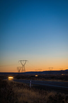 View of electricity transmission towers standing in a rural landscape at sunset with a road in the foreground under a clear gradient sky in Waiouru, Manawatu-Whanganui, New Zealand.