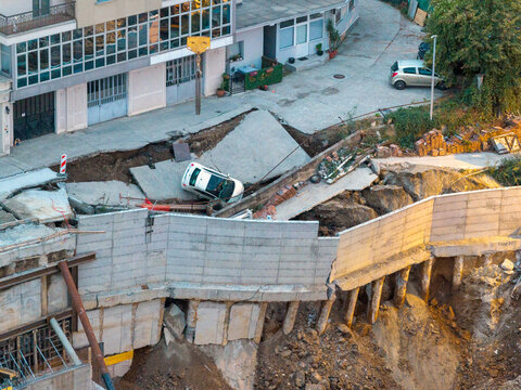 Belgrade, Serbia - 23 September 2026: Aerial view of a construction site collapse with a car partially fallen into a sinkhole, showing exposed concrete retaining walls, soil, and debris.