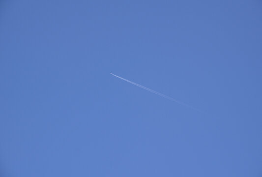 Passenger airplane flying high in clear blue sky leaving a white condensation trail behind.