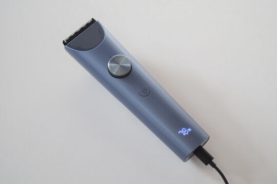 Modern cordless electric hair clipper charging with cable and LED battery indicator on white background