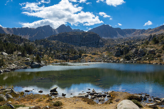 View of Llac de Pessons surrounded by rocky mountains and alpine terrain under a clear blue sky in Grau Roig, Encamp, Andorra.