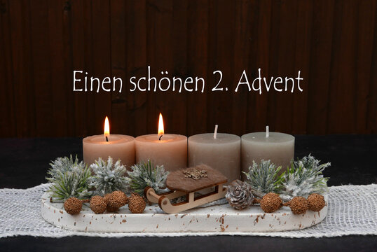 Rustikales Adventsgesteck mit zwei brennenden Kerze. Zweigen  und Holzschlitten zum 2. Advent.
