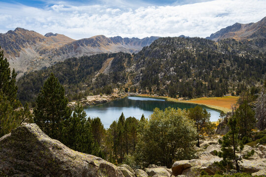 View of Llac de Pessons surrounded by pine trees, rocky terrain, and mountain peaks in Grau Roig, Encamp, Andorra.