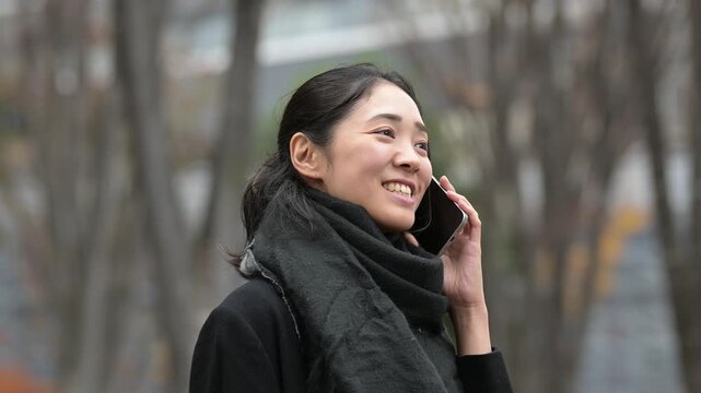 冬の屋外で笑顔でスマートフォンで通話をする30代日本人女性