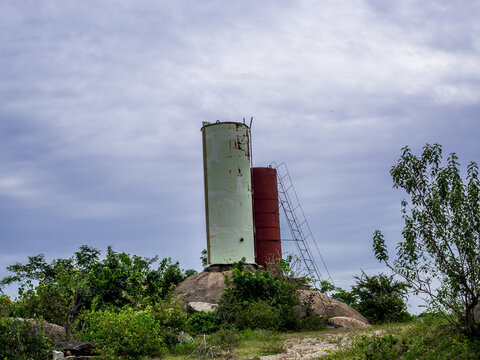 View of two industrial silos, one light green and one red, standing on a rocky outcrop amidst lush vegetation and rolling hills in Shere Hills, Plateau, Nigeria.