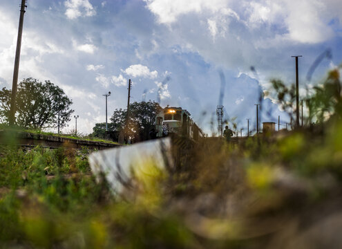 View of a train moving along the railway tracks with a person walking nearby under a cloudy sky in Jos, Plateau, Nigeria.