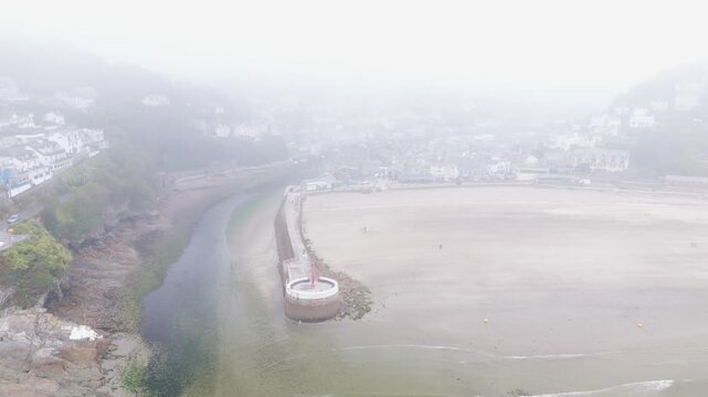 Aerial view of the misty Looe beach and harbour with stone pier and coastal town buildings in Looe, England, United Kingdom.