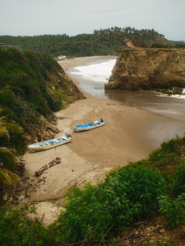 View of El Bejuco beach with two small fishing boats resting on the sand, surrounded by rocky cliffs and lush tropical vegetation in Lazaro Cardenas, Michoacan, Mexico.