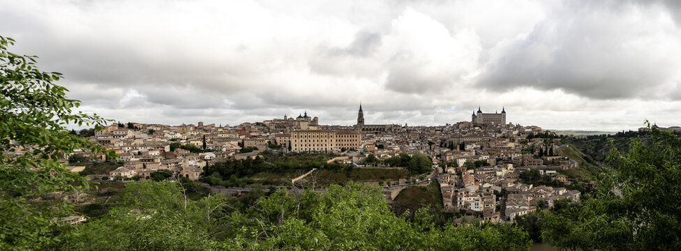 View of the historic skyline of Toledo featuring the cathedral and Alcazar under a cloudy sky in Toledo, Castile-La Mancha, Spain.