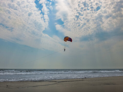 Small red parasail flying high above the sea under a dramatic cloudy sky