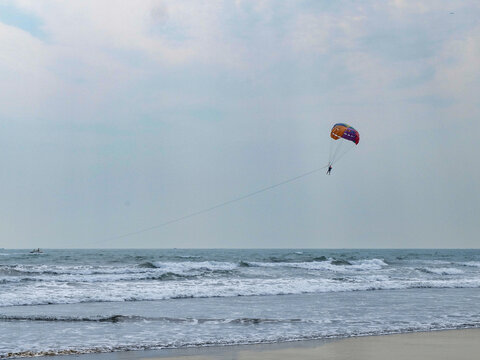 Lone red parasail high in a hazy sky above rolling waves breaking toward the shore
