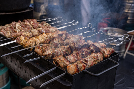 View of seasoned meat skewers grilling on a metal barbecue with rising smoke at a street food market in Vilnius, Vilnius County, Lithuania.