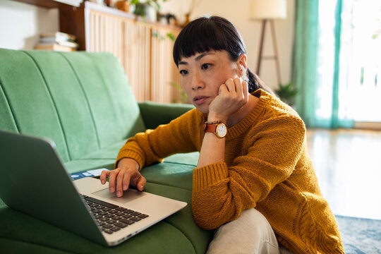 Pensive woman using laptop on the floor at home