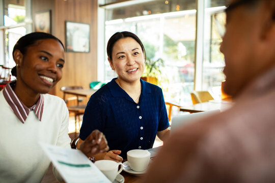 Two women discuss a document with colleague in a cafe