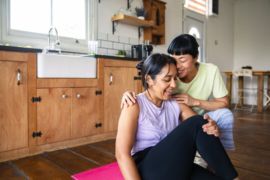 Two women sharing a supportive post-workout moment in a kitchen