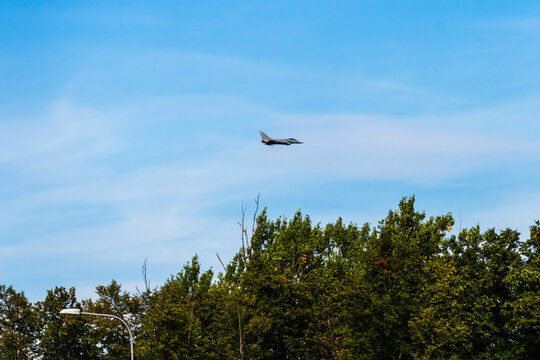 View of a fighter jet flying through a clear blue sky above a dense line of green trees in Mosnov, Moravian-Silesian Reg, Czechia.