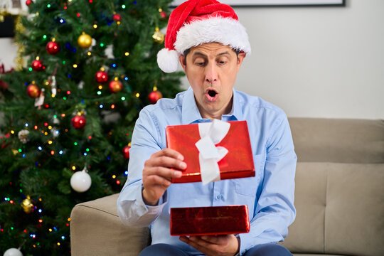 Wow, gift box and man in studio for christmas, festive or tradition celebration with light. Surprise, holiday and male person with present by xmas tree with omg expression at home