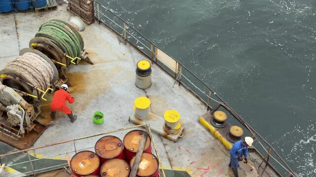 crew cleaning ship main deck at the aft mooring station by mops.