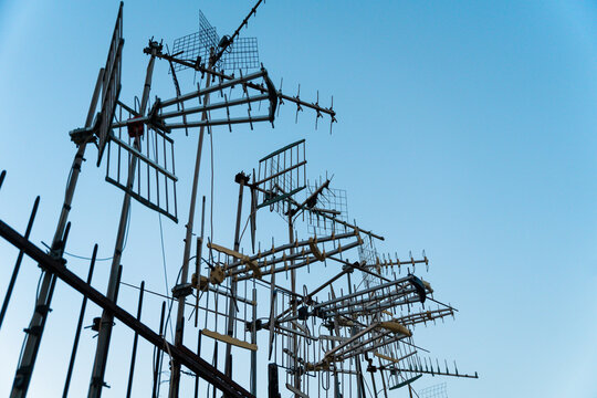 View of multiple television antennas mounted on a rooftop against a clear blue sky with a metal fence in the foreground in Naples, Campania, Italy.