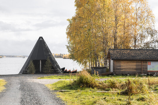 View of Apukka Resort with a traditional wooden kota shelter by the lake, surrounded by autumn foliage in Rovaniemi, Lappi, Finland.