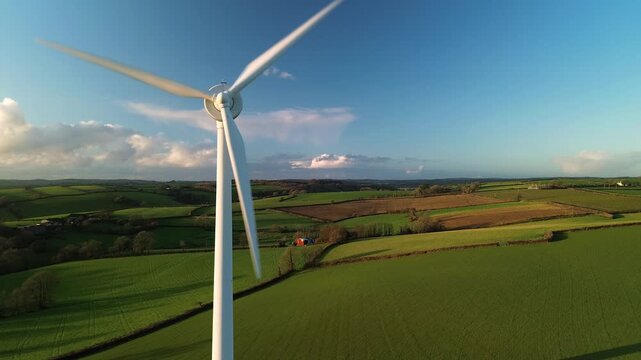 Aerial view of a rotating wind turbine generating clean sustainable energy above the green rolling hills of the Cornish countryside in Looe, England, United Kingdom.