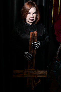 Woman in skeleton gloves holds an inverted wooden cross for Halloween