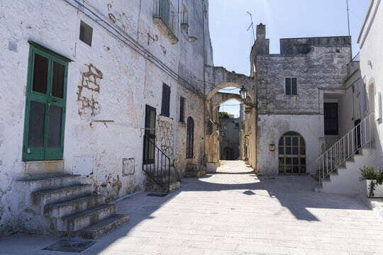 View of a narrow street with white-washed stone walls, a stone archway, and traditional architecture in the historic center of Ostuni, Apulia, Italy.