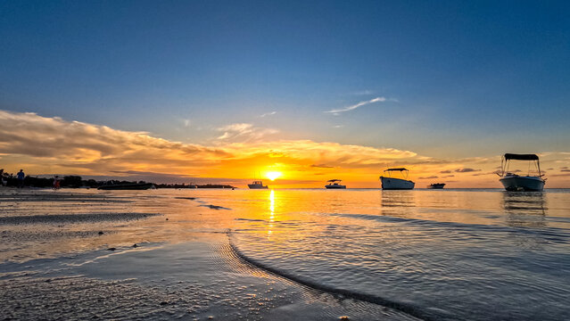 View of a golden tropical sunset over the Indian Ocean with small boats anchored in calm coastal waters in Trou-aux-Biches, Pamplemousses District, Mauritius.