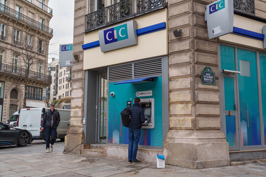 Paris, France - November 12 2025: A person uses a CIC bank ATM beside a historic Parisian street and ornate facade