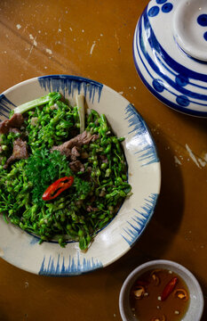 A vibrant plate of stir-fried thien ly flowers with beef, garnished with chili, served alongside a dipping sauce and traditional ceramic dishware.