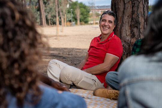 Happy mature man laughing with friends during outdoor picnic