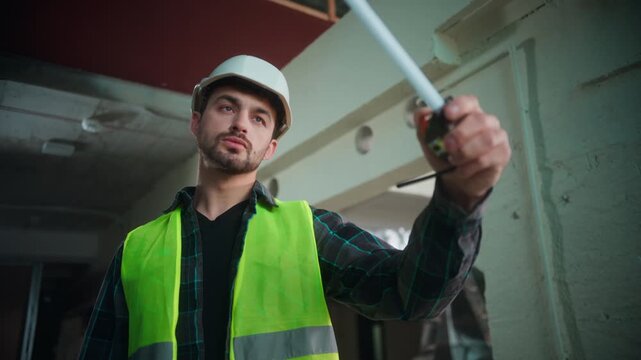 Professional Caucasian builder man measuring construction parts with tape male engineer uniform checking dimensions use tool foreman planning repair architecture project contractor inspection indoor